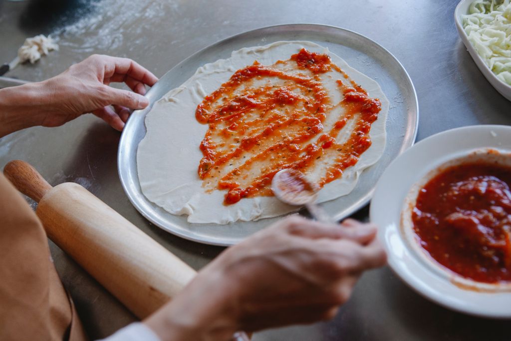 A detailed view of spreading tomato sauce on pizza dough, ready for baking.