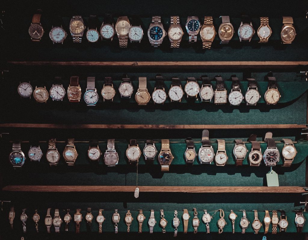 A diverse collection of vintage wristwatches lined on dark wooden shelves with ambient lighting.