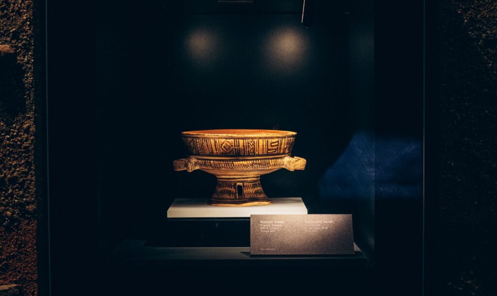 A golden vase exhibited in a Turkish museum, illuminated in a dark display case.