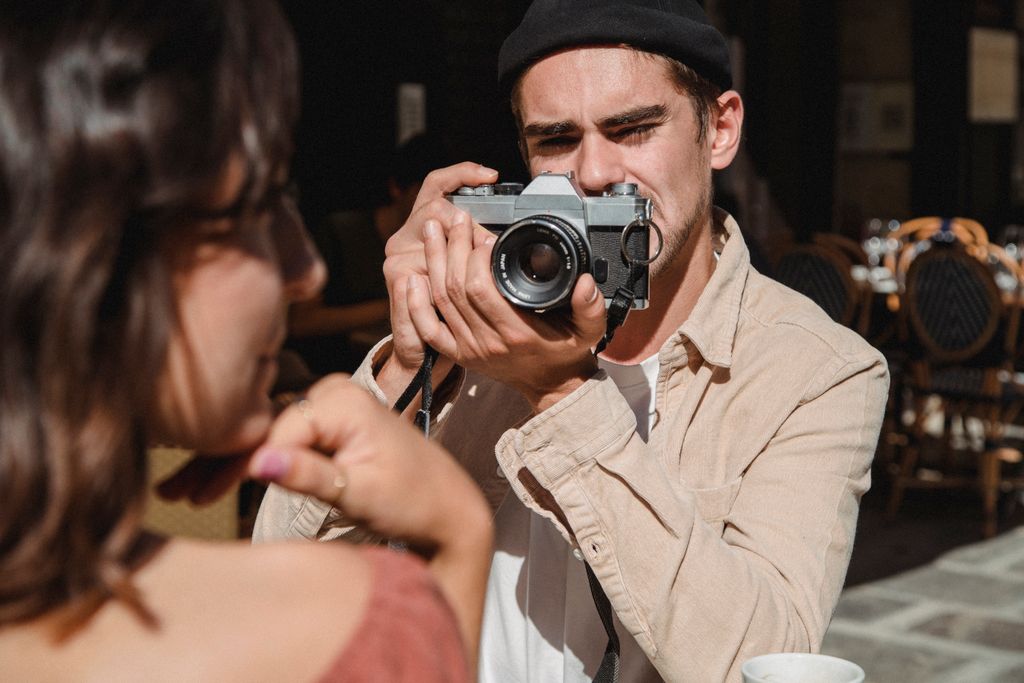 A man taking a photo of a woman with a vintage camera in an outdoor cafe setting.