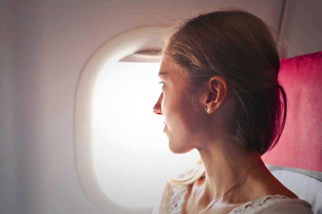 A woman gazes thoughtfully out the window of an airplane during her journey.