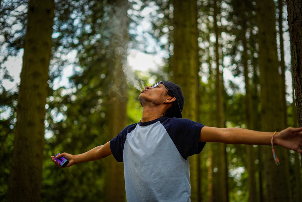 A young man stands in a forest with arms wide open, embracing the outdoors.