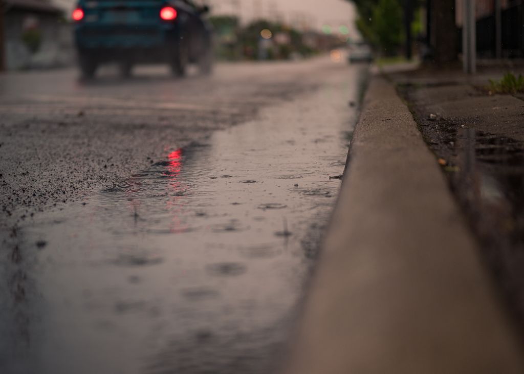 Moody urban street scene after rain with car on wet pavement. Captures city life in unique detail.