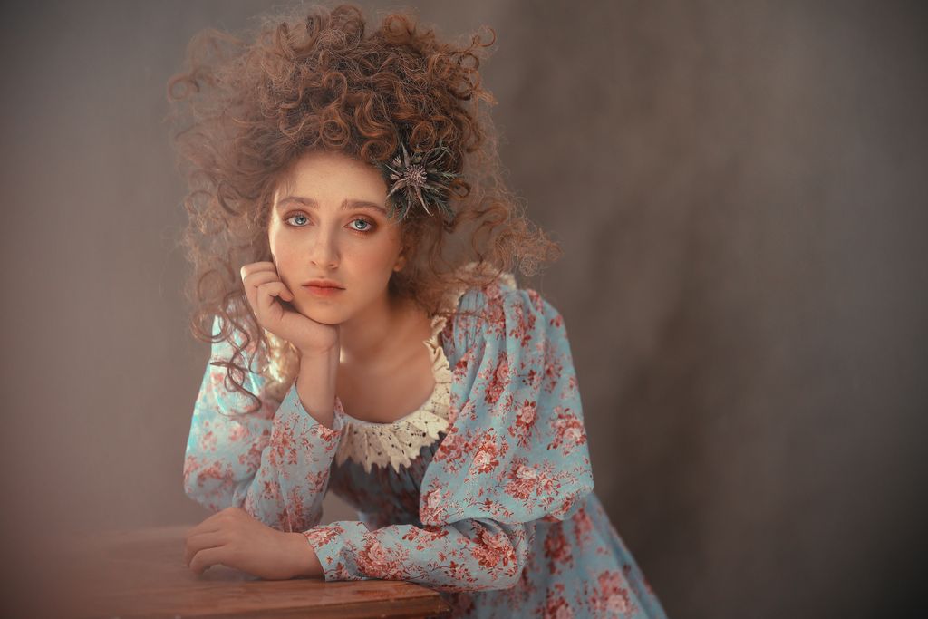 Portrait of a woman in vintage floral dress posing thoughtfully indoors.
