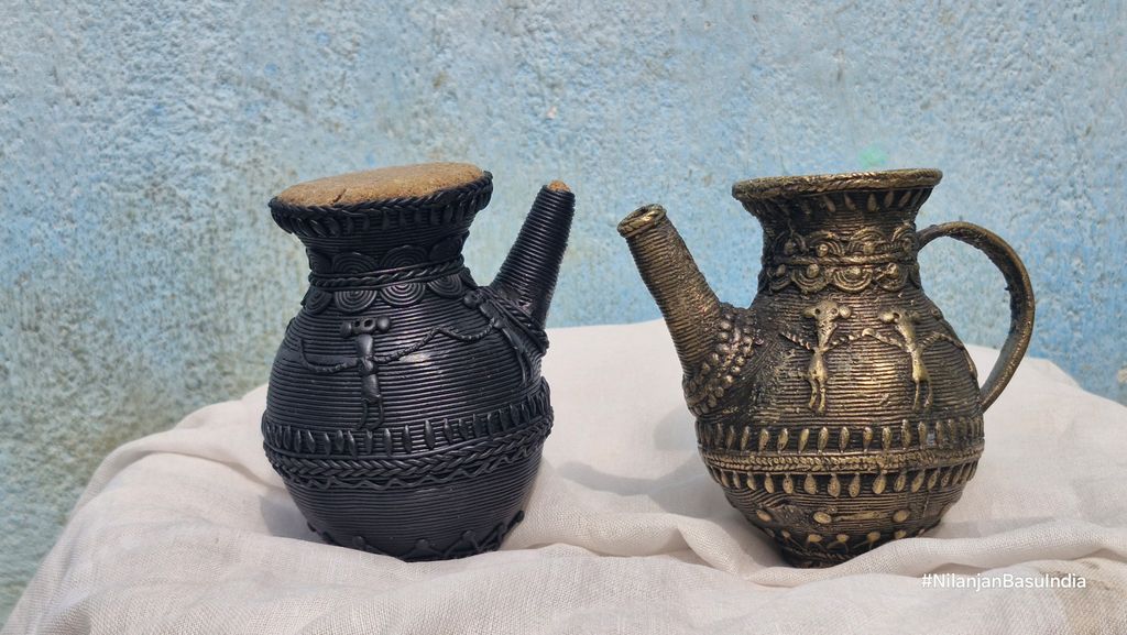 Two Dhokra art vessels displayed against a textured backdrop, highlighting intricate metalwork.