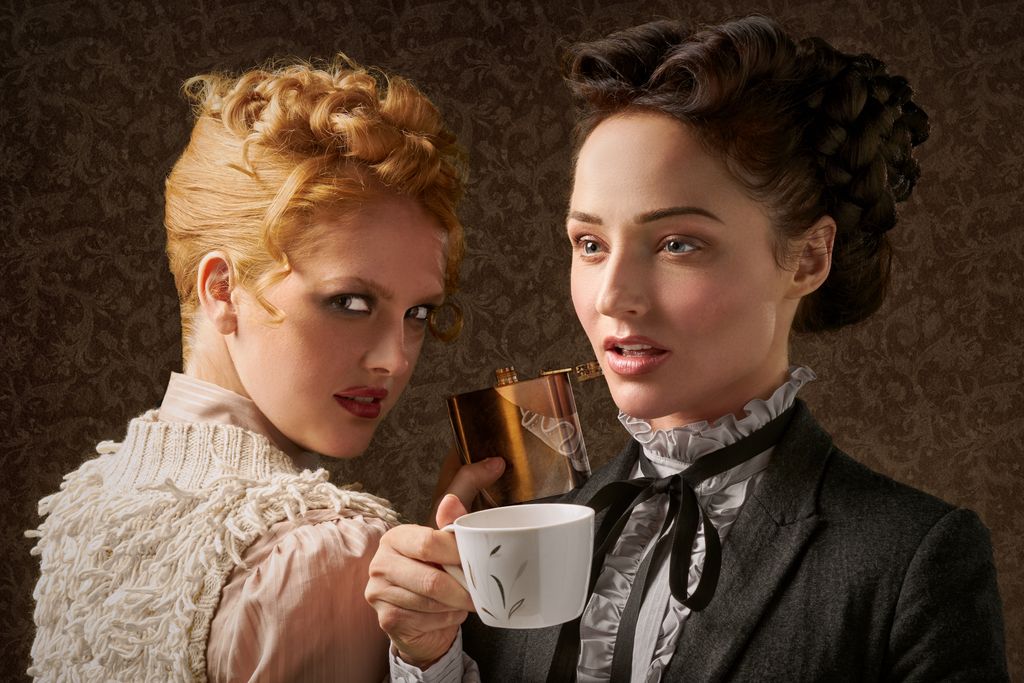 Two elegant women in vintage attire posing with a cup. A sense of classic style and graceful beauty.