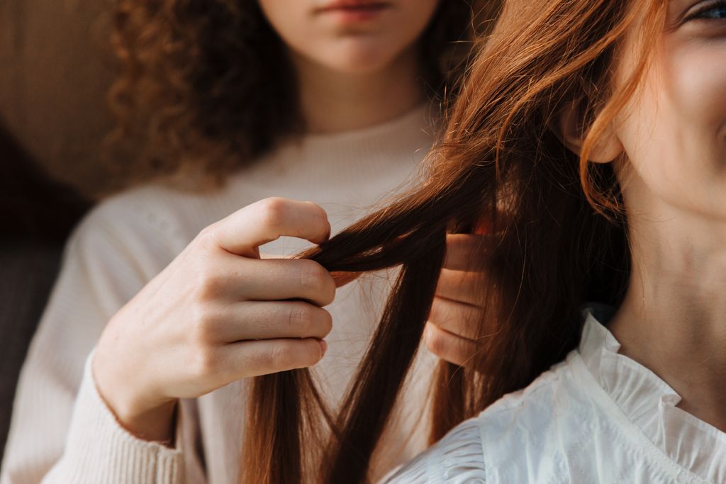Two women bonding as one braids the other's hair, symbolizing friendship and beauty.